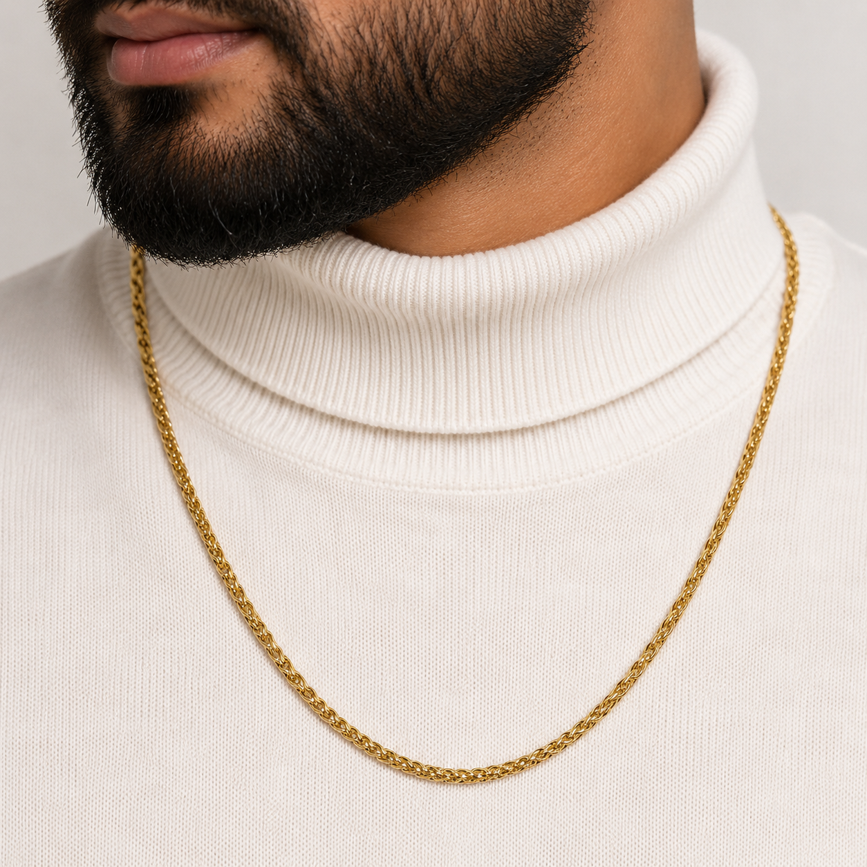 A close-up of a man wearing a gold chain necklace over a white ribbed turtleneck sweater.