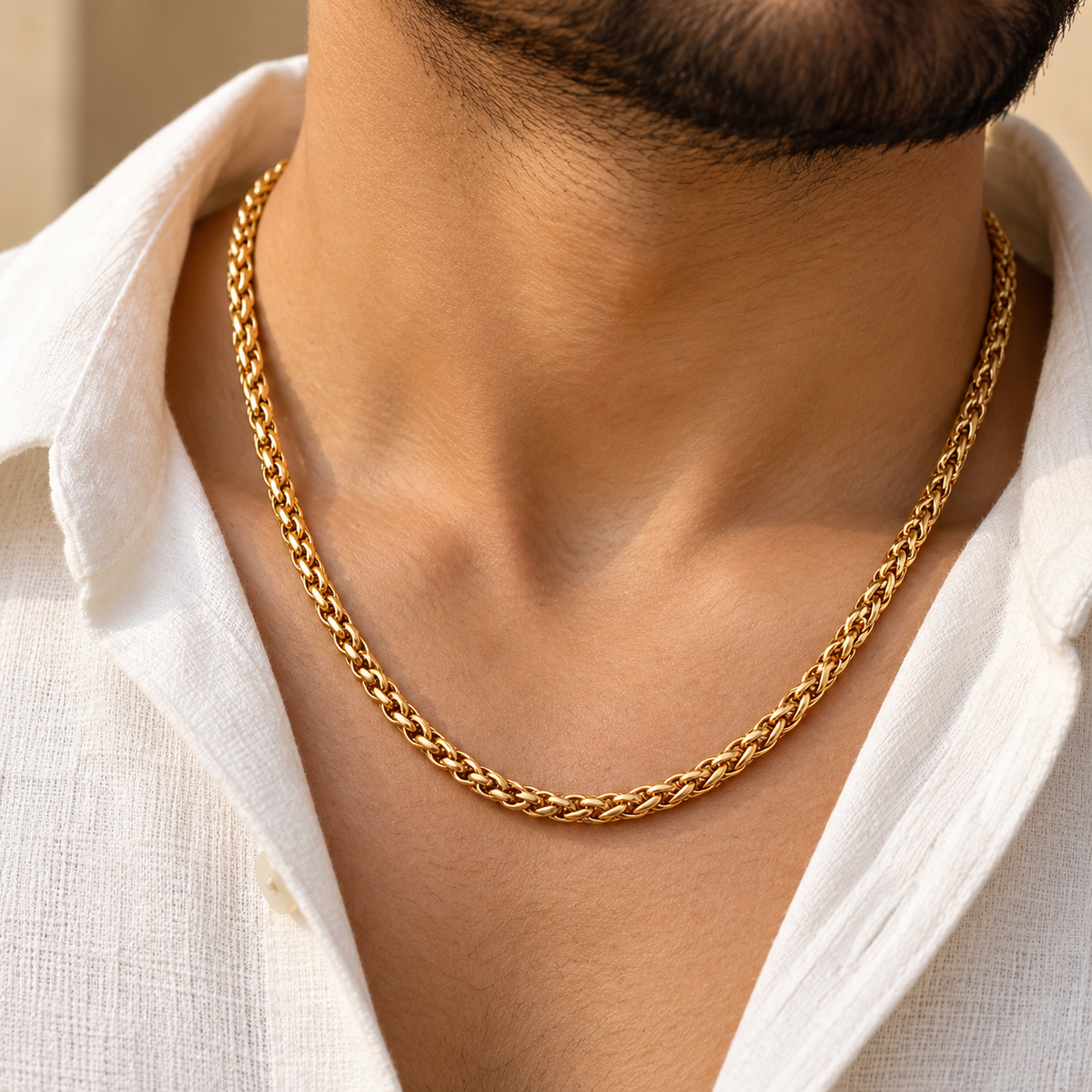 A close-up of a man's neck and chest wearing a thick, shiny gold chain necklace over a white collared shirt.